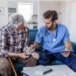 home health care provider monitors the blood pressure of an elderly client in their living room.