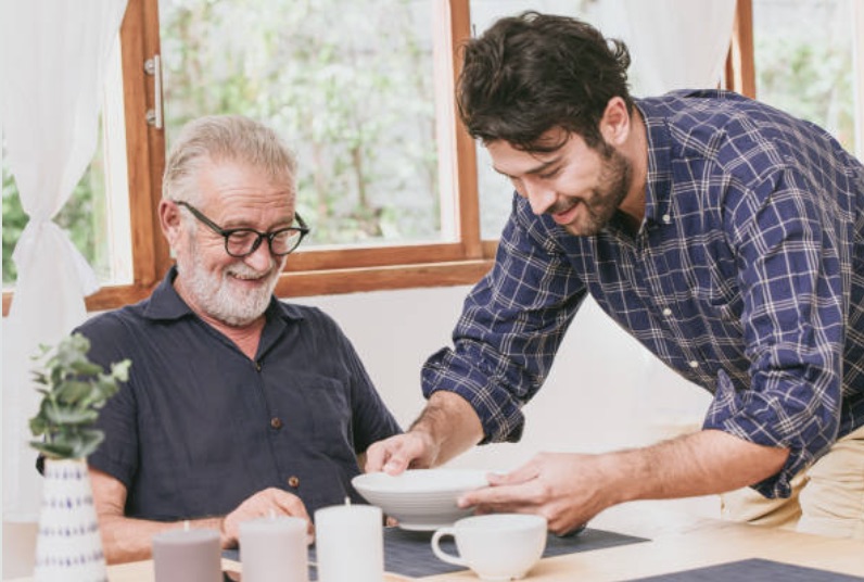 In a heartwarming scene, Young man serving food to elderly father care at home happy smiling.<br><br>